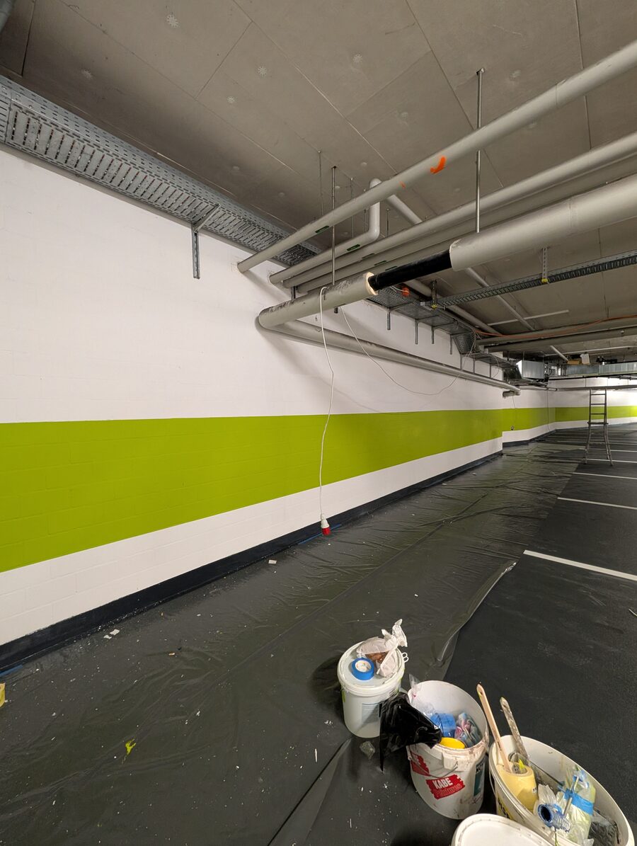 Tiefgarage mit weisser Wand und grün gestrichenem Streifen, Farbeimer auf abgedecktem Boden