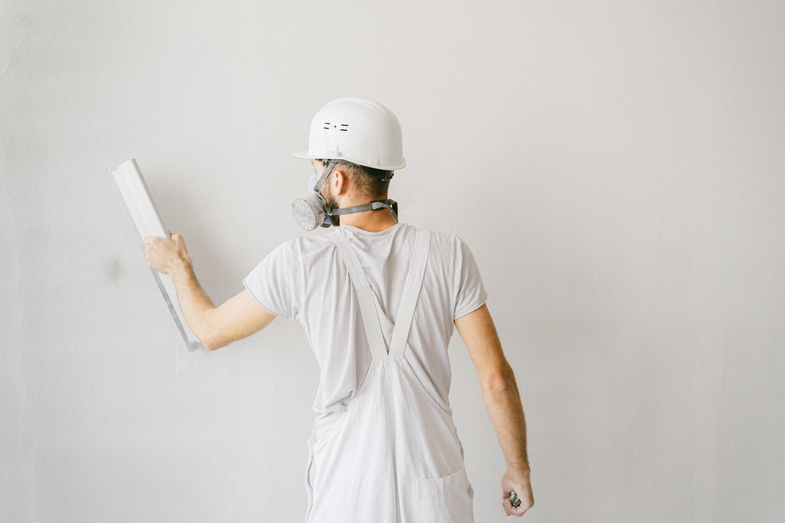 Maler in weisser Arbeitskleidung mit Helm rollt eine helle Wand