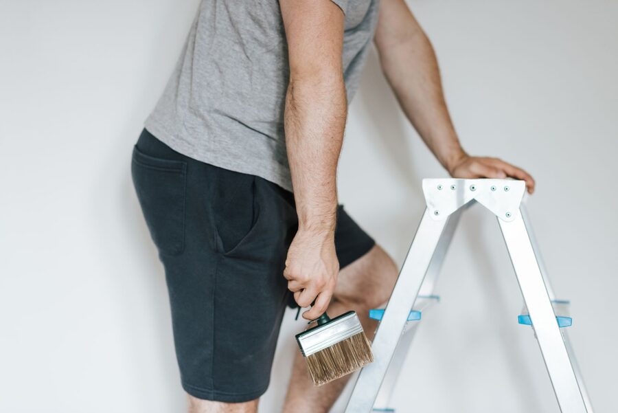 Handwerker steht mit Flachpinsel an einer Leiter