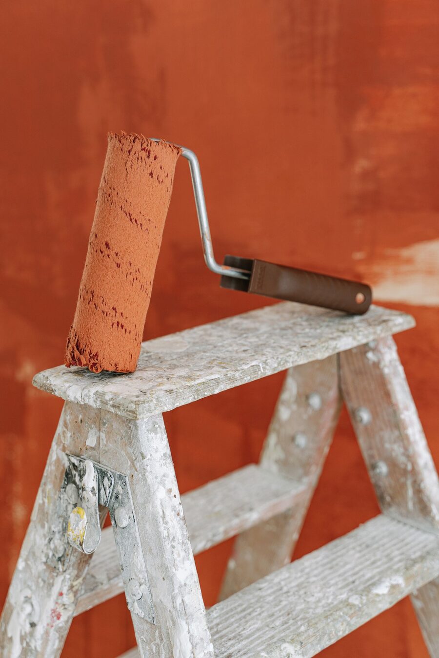 Farbroller mit orangeroter Farbe auf einer Trittleiter vor halb gestrichener Wand